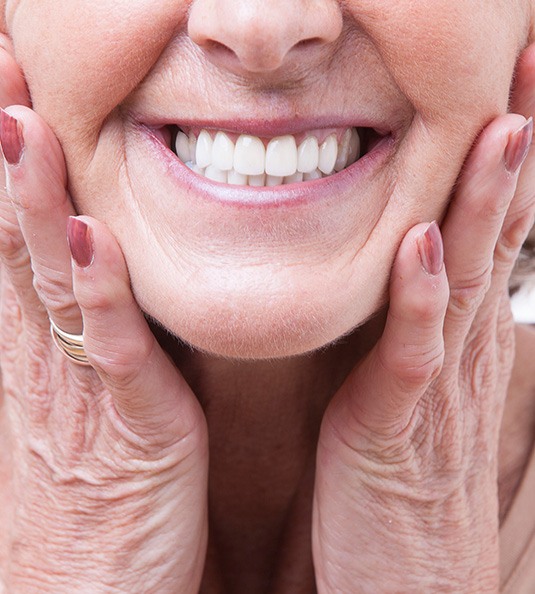 Nose-to-neck view of older woman placing hands on her jaw smiling