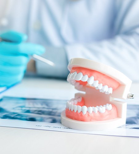 Dentist in blue gloves examining X-ray with artificial teeth on desk