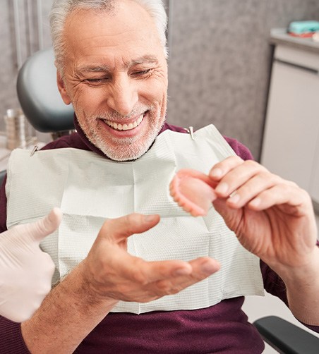 Man in maroon sweater receiving dentures from dentist giving thumbs up