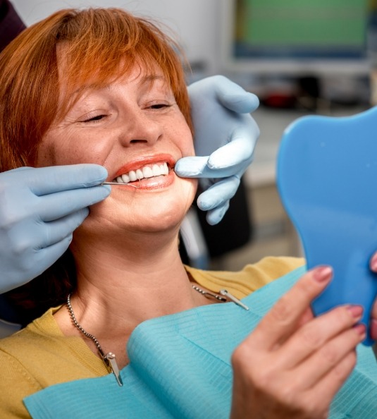 Woman with red hair sitting in dental chair checking smile in mirror