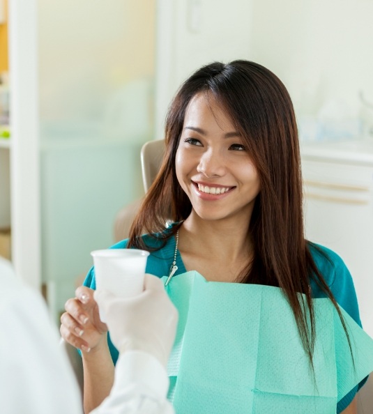 Female dental patient about to take cup from dentist