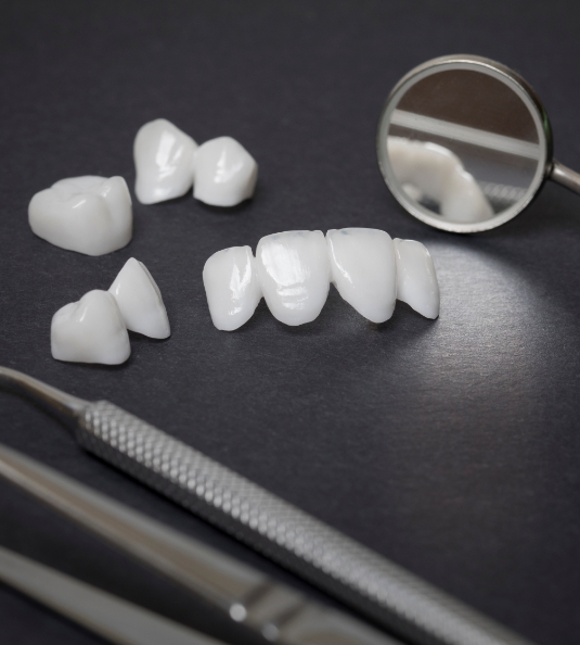 Metal free restorations sitting on black surface next to dental instruments