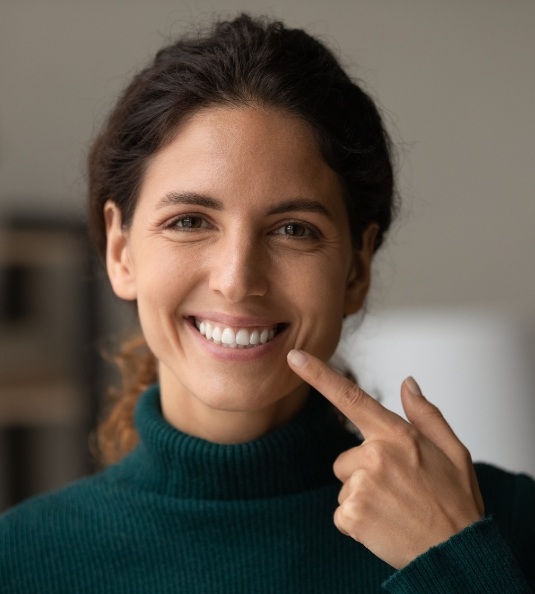 Woman in blue turtleneck sweater pointing to smile