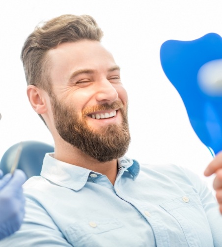 Male patient in button up shirt checking smile in mirror