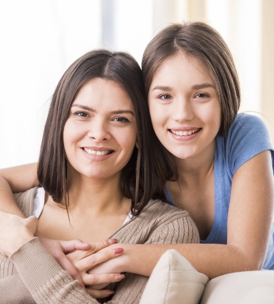 Woman sitting on couch hugged from behind by another woman