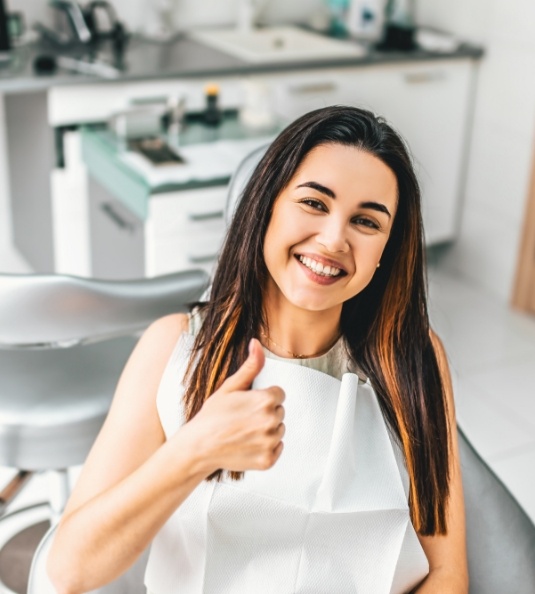 Woman sitting in dental chair and giving thumbs up