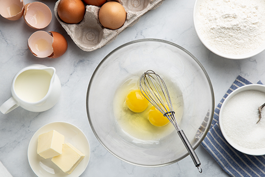 Egg in bowl with whisk surrounded by other ingredients