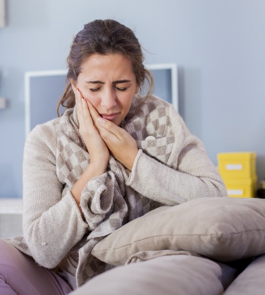 Woman with sweater in bed rubbing jaw in pain