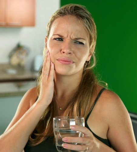 Woman rubbing jaw in pain and holding glass of water