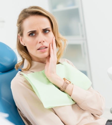 Woman in dental chair rubbing jaw and looking concerned