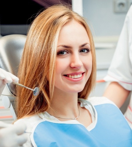 Woman sitting in dental chair smiling with dentists nearby