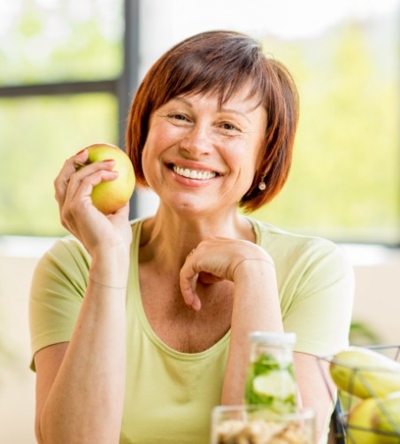 Woman in green shirt smiling and holding apple