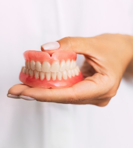 Close up of hand holding full dentures in Carrollton