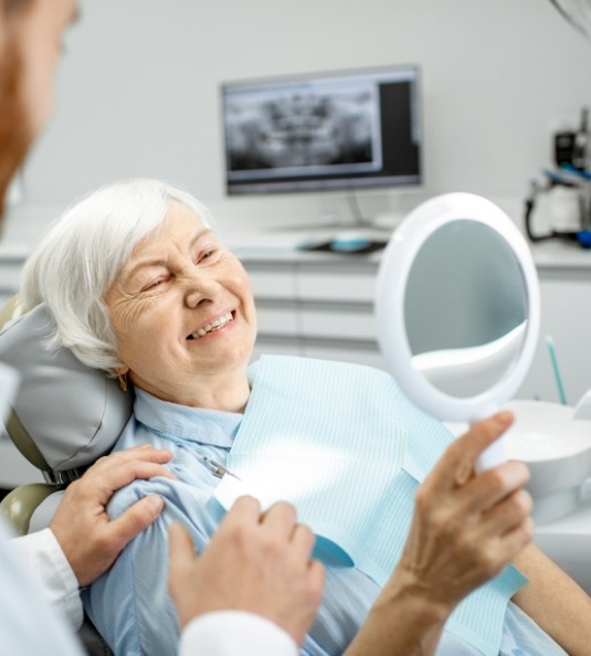 Senior woman in dental chair checking smile in mirror