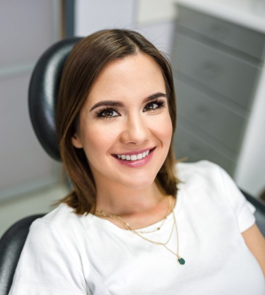 Woman in white shirt sitting in dental chair and smiling