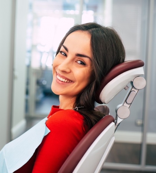 Woman in red shirt sitting in dental chair and smiling