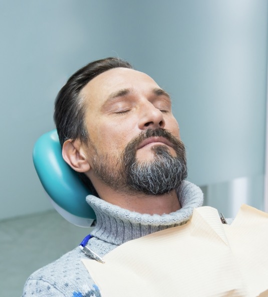 Man in sweater sitting back in dental chair and relaxing