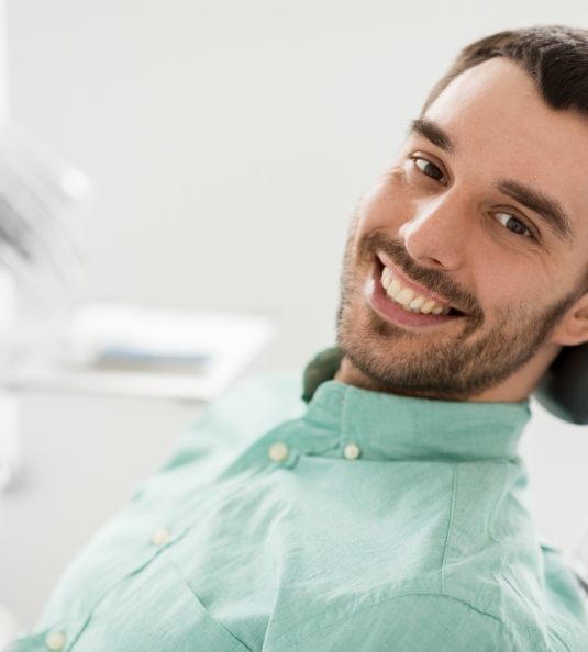 Man in green shirt sitting in dental chair and smiling