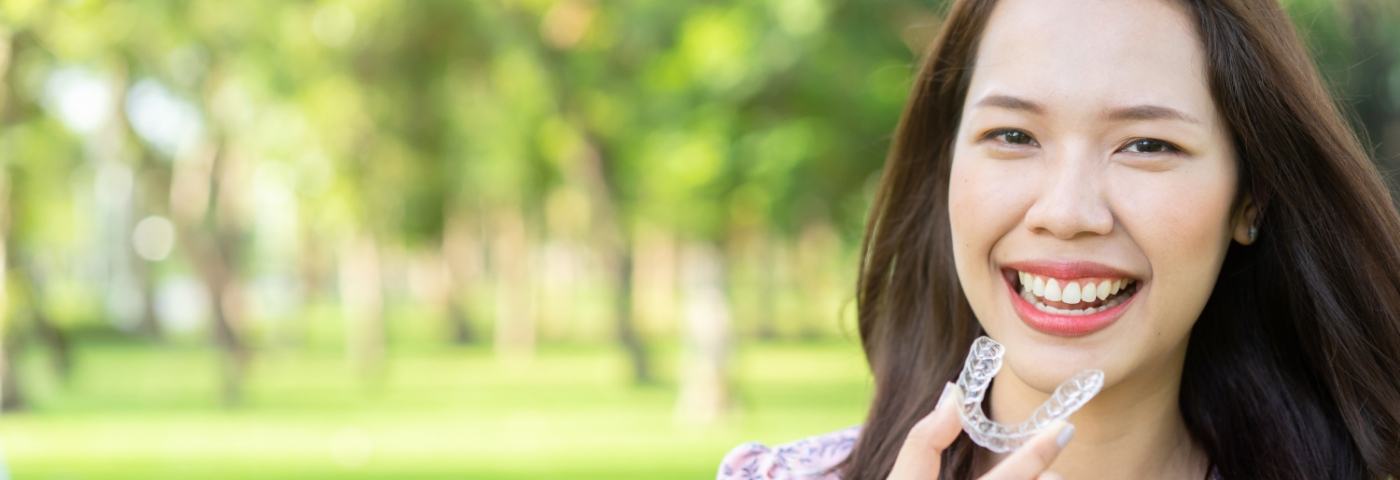 Woman in park about to put in Invisalign in Carrollton