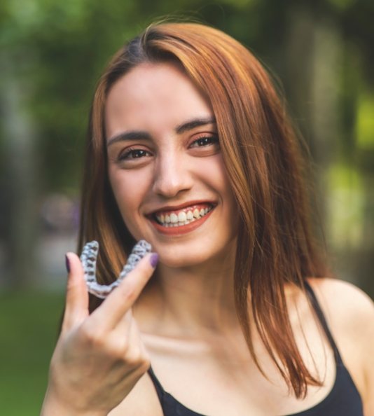 Red haired woman holding clear aligner and smiling