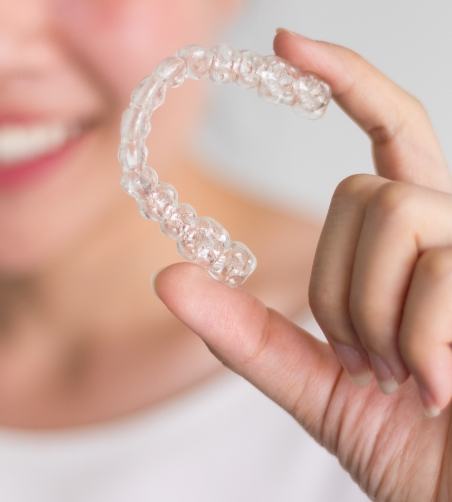 Woman holding a clear aligner and smiling