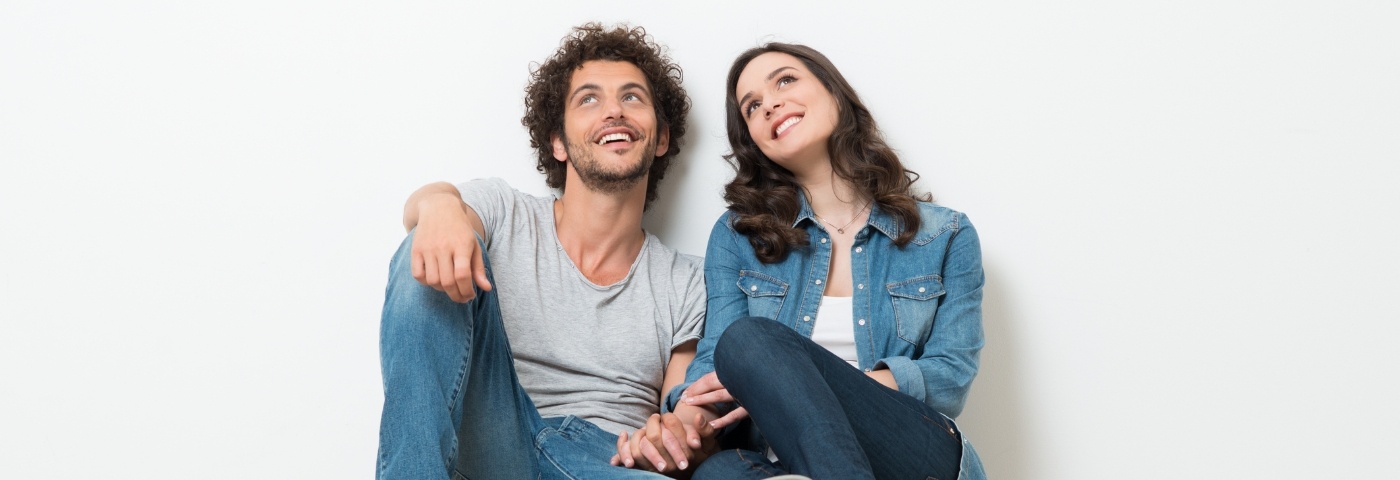 Man and woman sitting against wall smiling