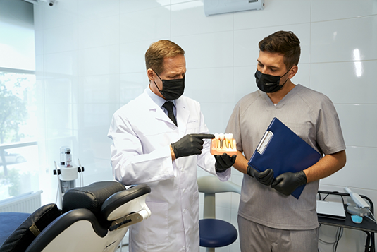 Periodontist showing patient model of dental implant