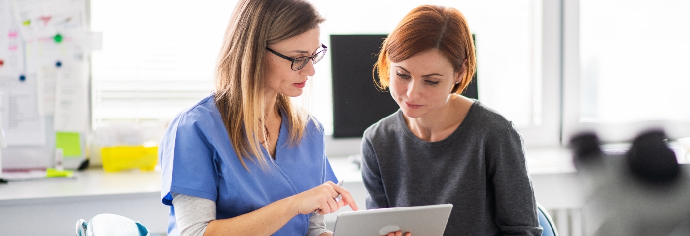 Female dentist showing female patient something on tablet