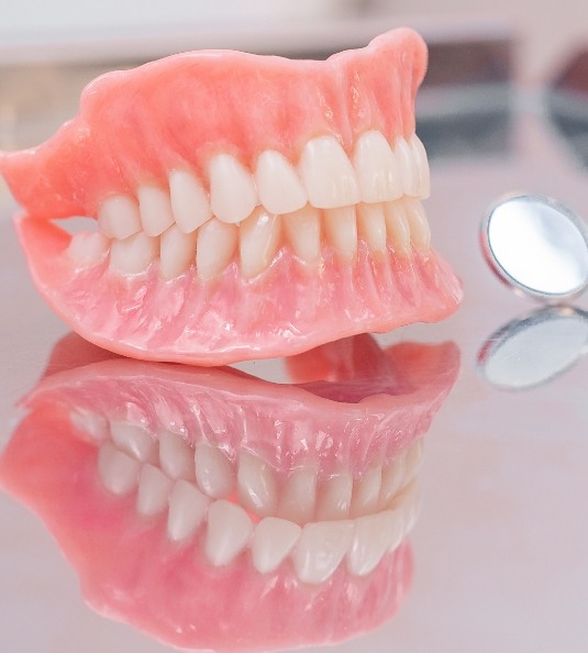 Illustration of full dentures sitting on reflective surface next to dental mirror