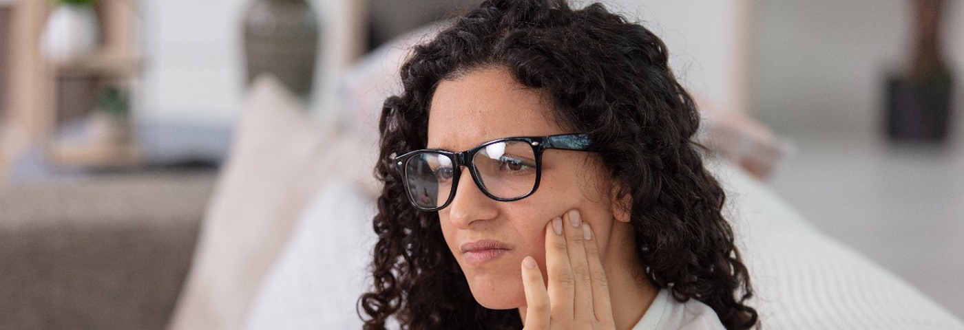 Concerned woman with glasses sitting on couch and rubbing jaw