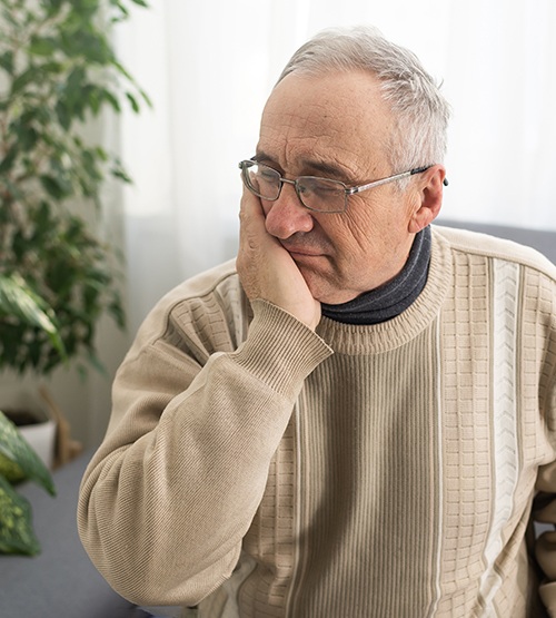 Man with glasses and sweater rubbing jaw