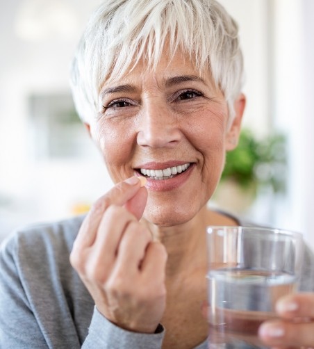 Senior woman holding glass of water and pill