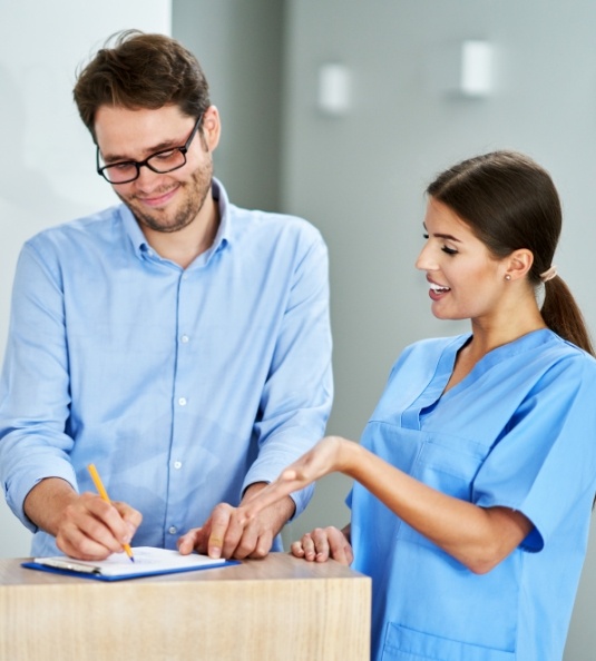 Female dental team member helping male patient fill out form