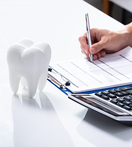 Writing on notepad with calculator and model tooth nearby