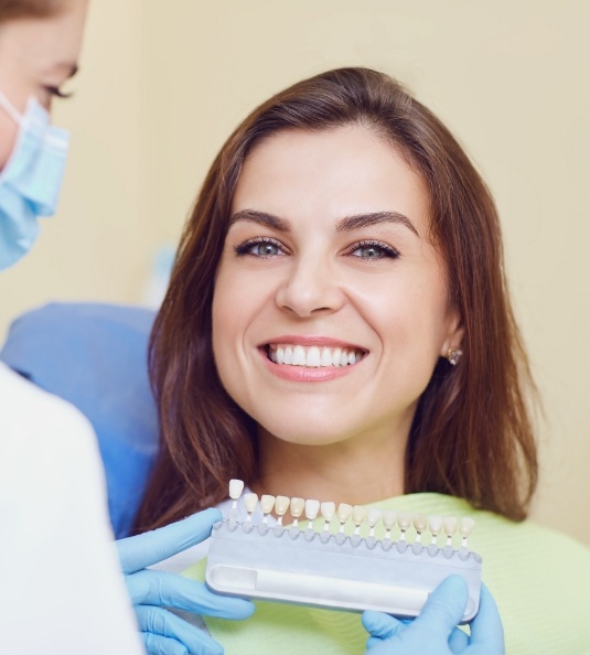 Woman sitting in dental chair while dentist holds shade matching tool