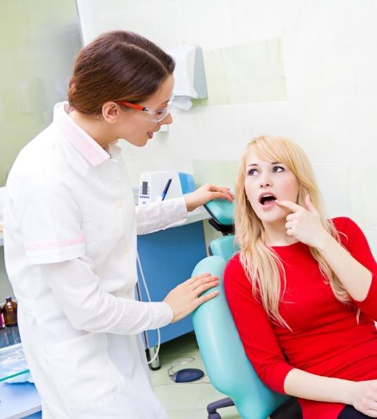 Female dental patient pointing to mouth and talking to dentist