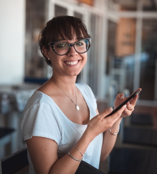 Woman with glasses holding phone and smiling