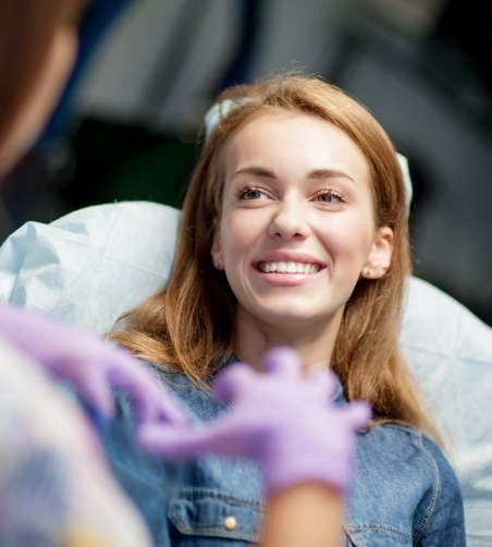 Woman in dental chair smiling and looking up at dentist