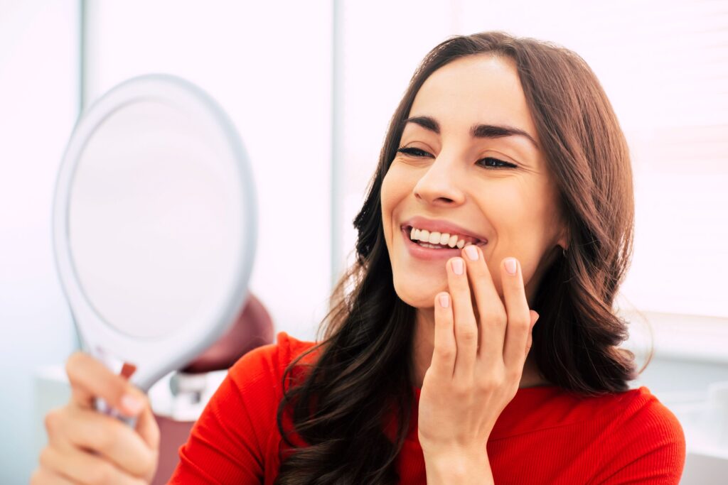 Woman in red shirt smiling at reflection in hand held mirror