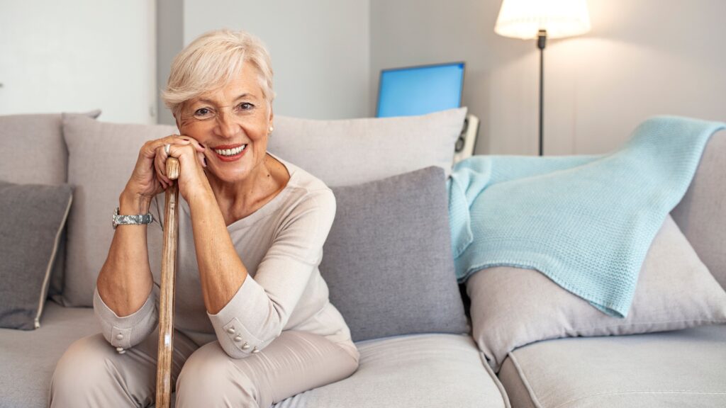 Woman sitting on beige couch smiling leaning on wooden cane